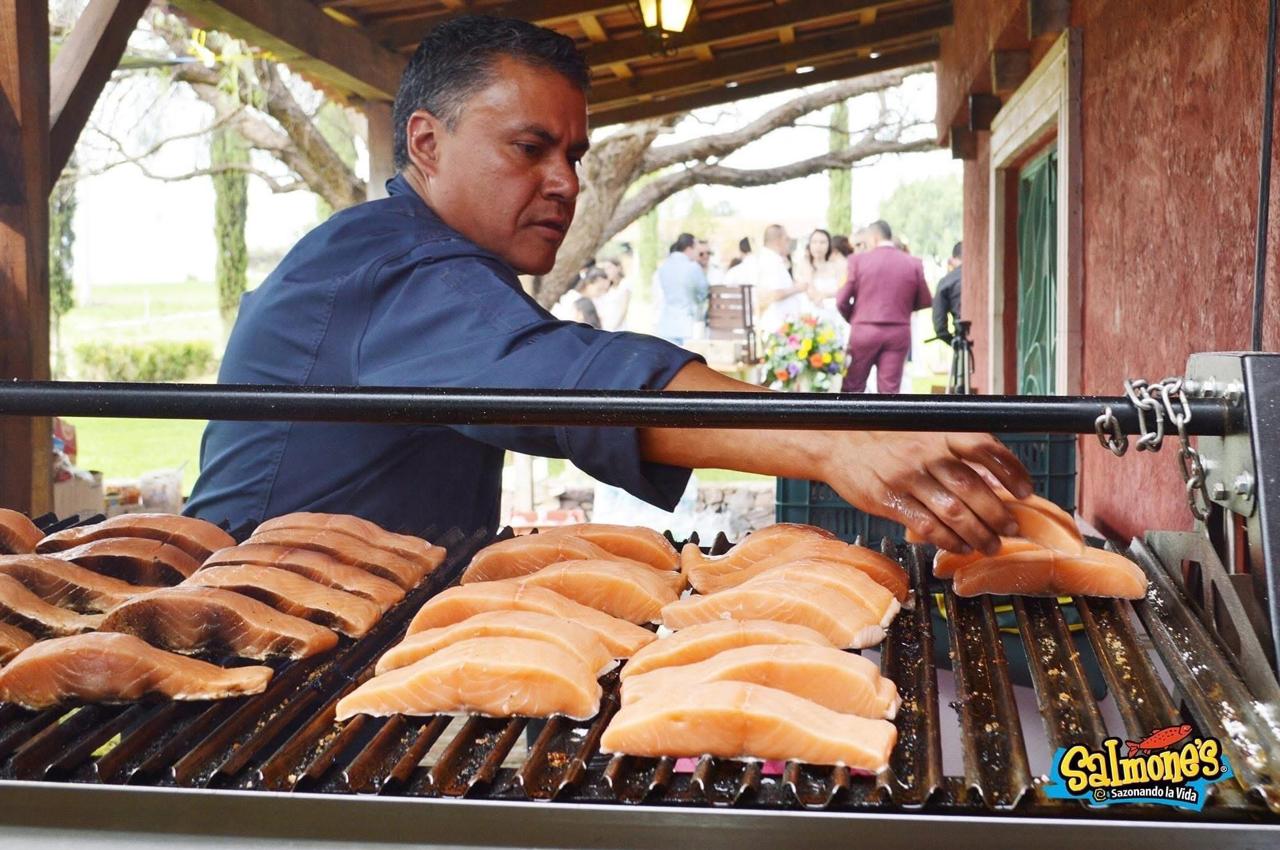 Cocinero asando filetes de salmón a las brasas en un evento
